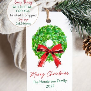 May include: A white gift tag with a watercolor wreath and red bow design. The tag reads "Merry Christmas" and includes a family name and the year 2022. Tag size is 2x3.5 inches.