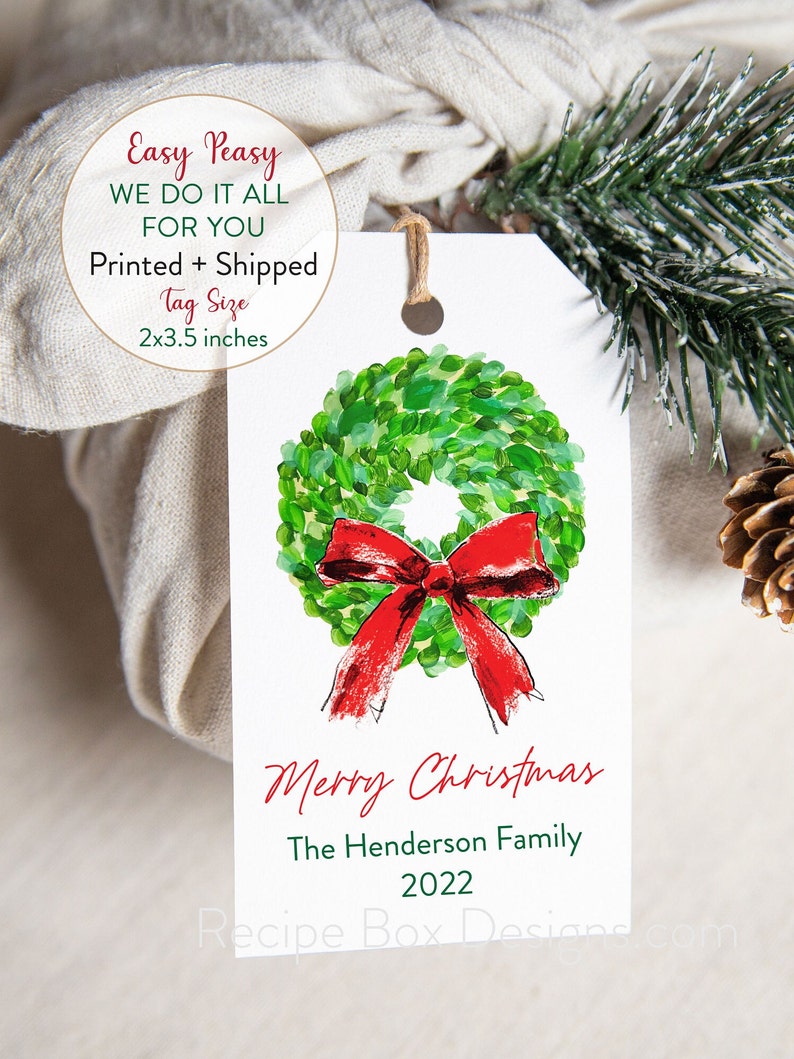 May include: A white gift tag with a watercolor wreath and red bow design. The tag reads "Merry Christmas" and includes a family name and the year 2022. Tag size is 2x3.5 inches.
