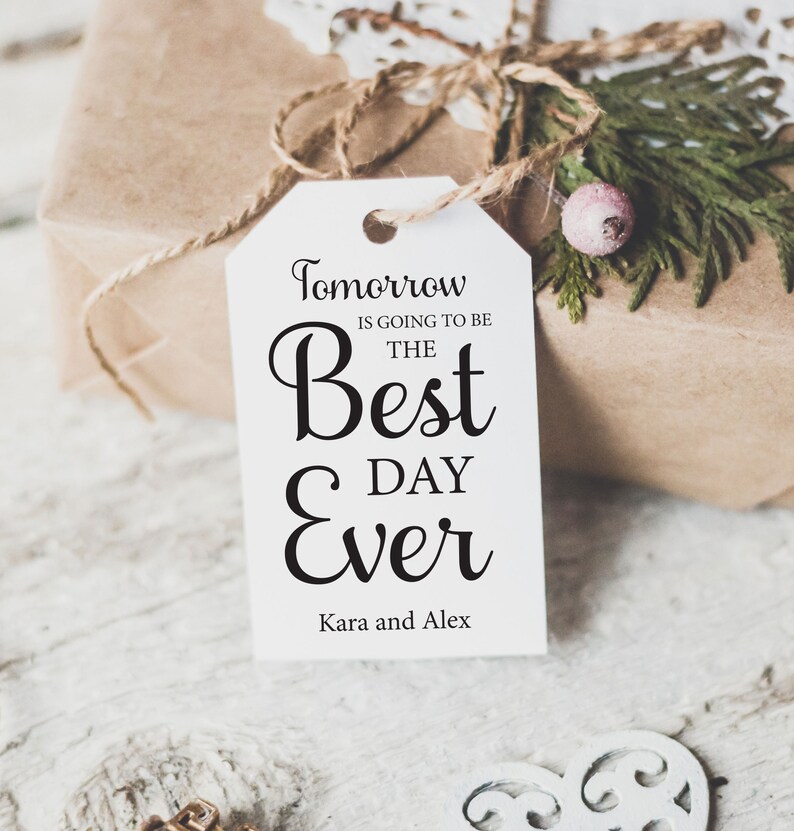 K&ouml;nnte beinhalten: Wei&szlig;er Geschenkanh&auml;nger mit schwarzem Text, der "Morgen wird der beste Tag aller Zeiten" und "Kara und Alex" lautet.