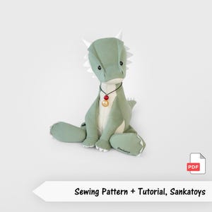 Puede incluir: Un peluche de dragón verde salvia con detalles blancos en cuernos y espina dorsal. El dragón tiene una barriga color crema y un collar con cuentas rojas y doradas. El texto "Sewing Pattern + Tutorial, Sankatoys" está en la parte inferior.