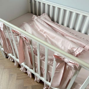 A white crib with a pink blanket and bows on the railings.