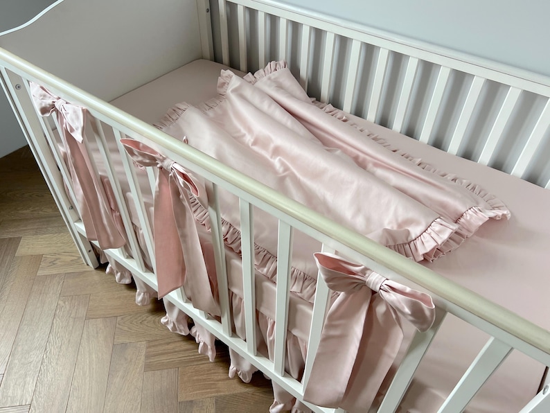 A white crib with a pink blanket and bows on the railings.