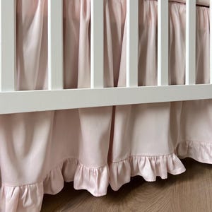 A white crib with pink ruffled curtains covering the sides.