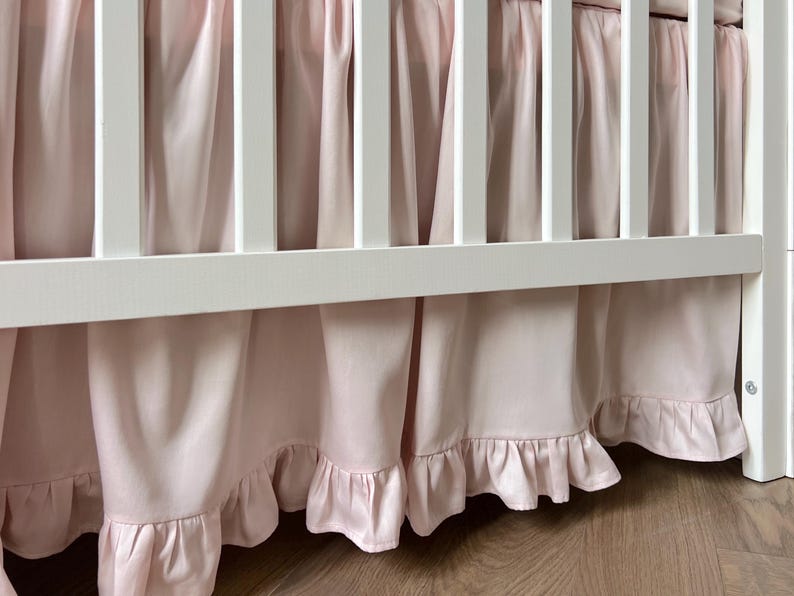 A white crib with pink ruffled curtains covering the sides.