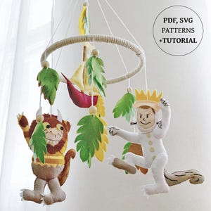 May include: A handmade baby mobile featuring felt characters from "Where the Wild Things Are." The mobile includes Max in a crown, a Wild Thing, a sailboat, and green and yellow felt leaves. The text "PDF, SVG PATTERNS +TUTORIAL" is in a circle.