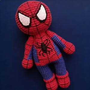 May include: A handmade crochet Spider-Man doll. The doll features a red and blue color scheme, with white eyes and a black spider emblem on the chest. The doll is approximately 8 inches tall.