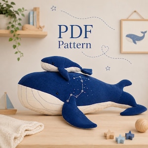 Op de afbeelding: Een grote donkerblauwe corduroy walvis knuffel met een crèmekleurige buik en een kleinere bijpassende walvis knuffel erbovenop. De grote walvis heeft witte geborduurde sterrenbeelden op de zijkant. De tekst luidt PDF Pattern.