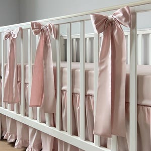 A white crib with pink ribbons hanging from the rails.