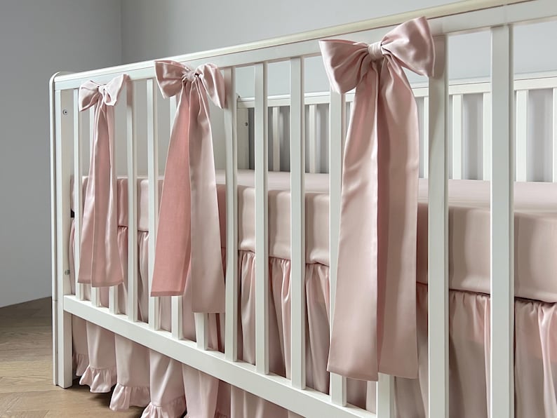 A white crib with pink ribbons hanging from the rails.