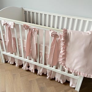 A white crib with pink ruffled bedding and bows on the railings.