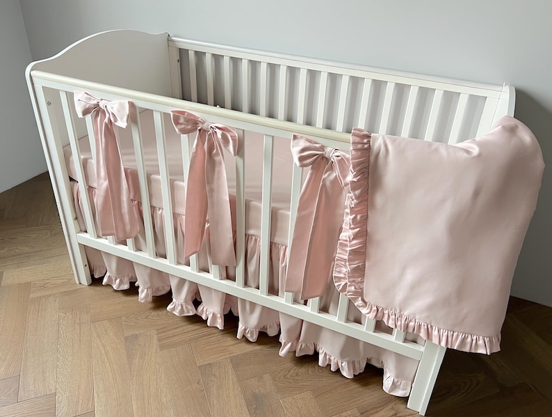 A white crib with pink ruffled bedding and bows on the railings.