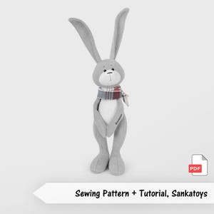 May include: A grey plush bunny with long ears and a plaid scarf. The bunny has a white belly and is wearing a scarf with red, white, and grey stripes. The text "Sewing Pattern + Tutorial, Sankatoys" is at the bottom.