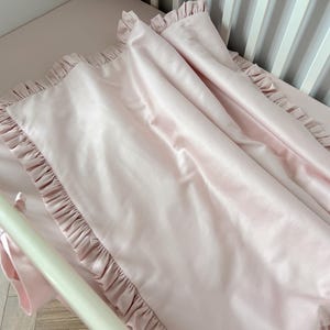 A pink, ruffled blanket is draped over a white crib, creating a cozy and inviting atmosphere.