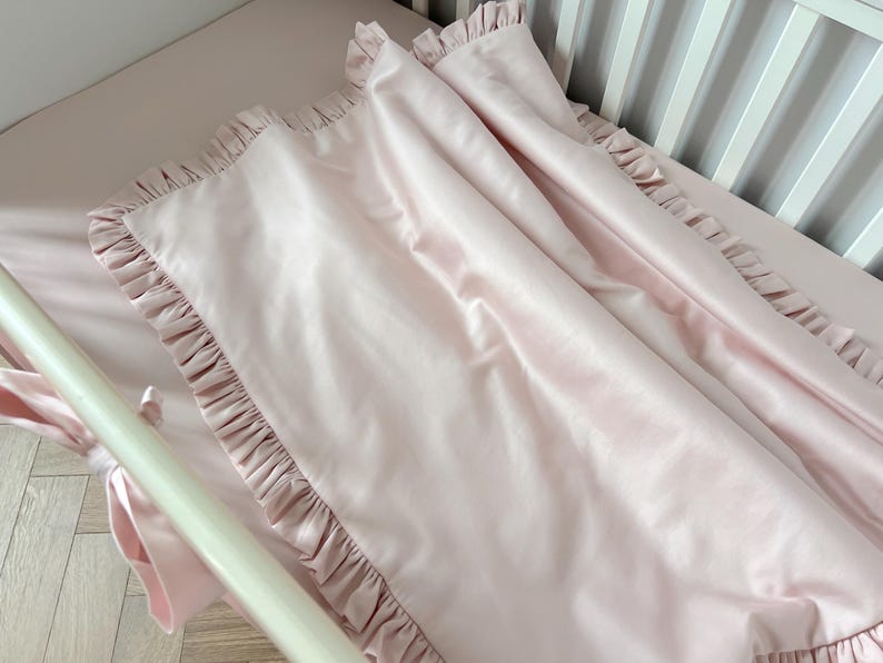 A pink, ruffled blanket is draped over a white crib, creating a cozy and inviting atmosphere.