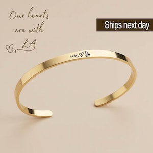 May include: Gold bangle bracelet with the inscription "we ♥ LA" engraved on the front.