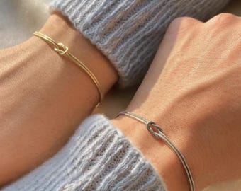以下が含まれることがあります： 結び目のデザインが施されたシンプルなブレスレットが2つ。1つはゴールド、もう1つはシルバーです。