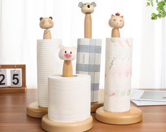 May include: Four wooden paper towel holders with different animal designs. The holders are made of natural wood and have a simple, rustic design. Each holder features a different animal: a koala, a panda, a pig, and a cat. The holders are all on a wooden table.