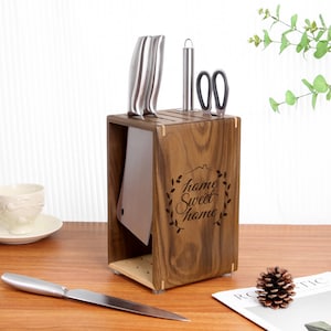 Könnte beinhalten: Ein Messerblock aus Holz mit dunkelbrauner Oberfläche. Der Block hat Schlitze für Messer und ein Fach für ein Hackmesser. Der Block hat die Worte "home sweet home" auf der Vorderseite eingraviert.