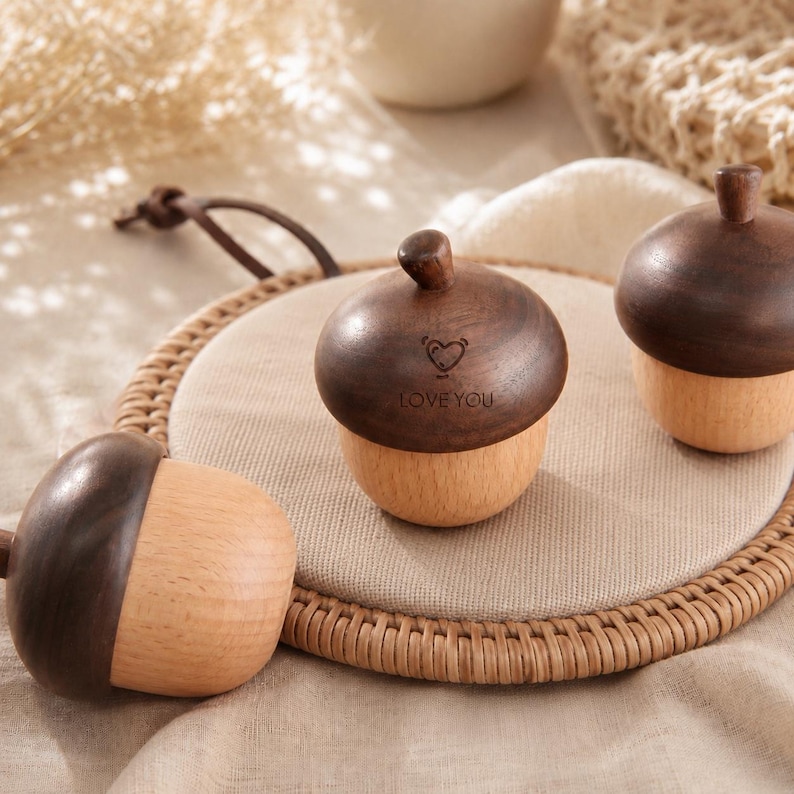 May include: Three wooden acorn-shaped containers with dark brown caps and light tan bases. The center acorn features a small engraved heart icon and the text LOVE YOU. Each piece has a smooth, polished finish and a rounded, functional design.