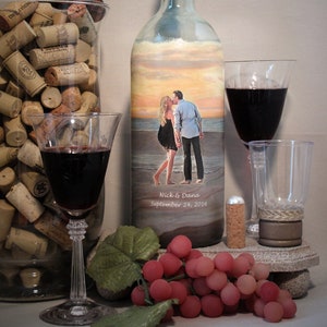 May include: A decorative wine bottle with a sunset scene and a couple kissing on the beach. The bottle has a black stopper and is next to a glass of red wine, a glass of water, and a bunch of grapes. The text "Nick & Dana September 24, 2016" is visible.