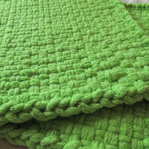 May include: Two green woven kitchen dishcloths or pot holders. The cloths are made of a thick, textured material and have a woven pattern.