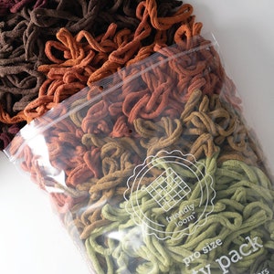 May include: A clear plastic bag filled with a variety of colors of yarn for crocheting. The yarn is in shades of brown, orange, yellow, and green. The bag has a label that says "friendly loom" and "pro size party pack".