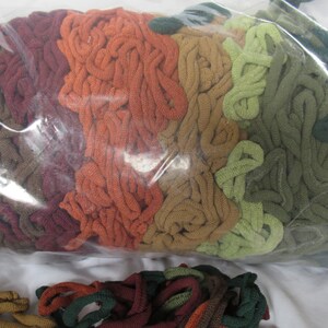 May include: A plastic bag filled with a variety of colorful yarn scraps in shades of brown, orange, green, and red. The yarn is arranged in a layered pattern, creating a visual effect of a rainbow.