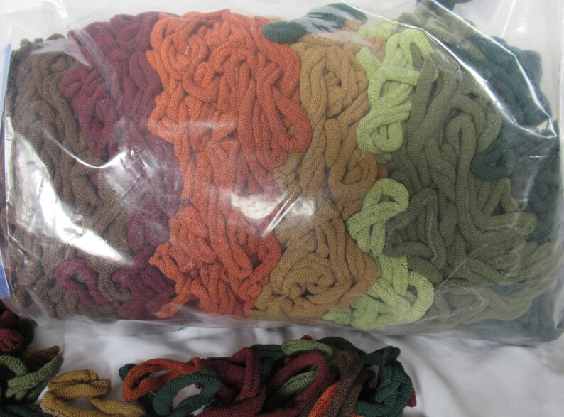 May include: A plastic bag filled with a variety of colorful yarn scraps in shades of brown, orange, green, and red. The yarn is arranged in a layered pattern, creating a visual effect of a rainbow.