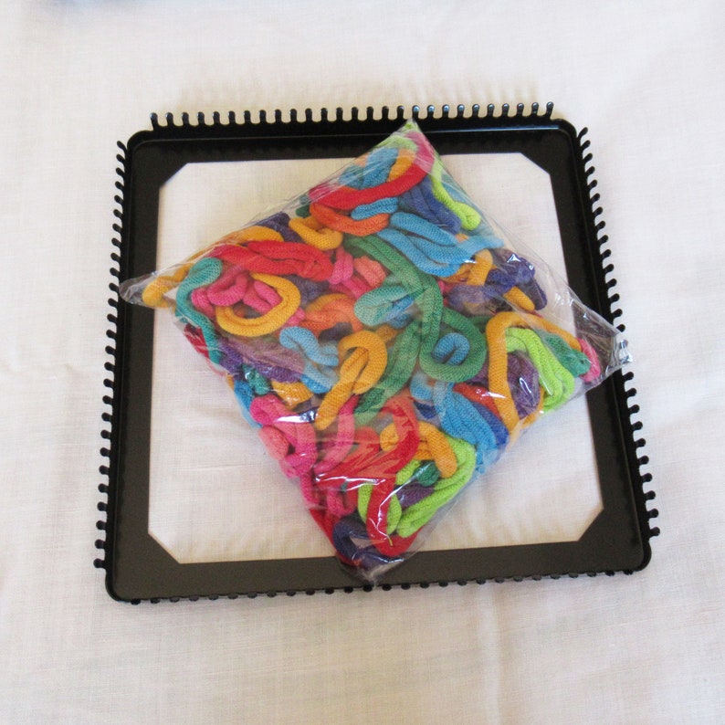 Puede incluir: Un telar de pl&aacute;stico negro con un surtido de hilo arco&iacute;ris en una bolsa de pl&aacute;stico. El hilo es de varios colores, incluyendo rojo, naranja, amarillo, verde, azul, morado y rosa.