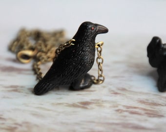 May include: A black crow pendant necklace with a gold chain. The crow has red eyes and is perched on the chain.