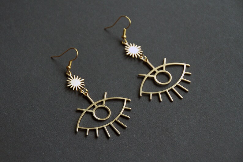 May include: Gold tone eye-shaped earrings with a white star charm dangling from each earring.