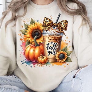 Puede incluir: Sudadera color crema con un gráfico temático de otoño. El diseño incluye una calabaza, girasoles y una bebida de café con crema batida y un lazo con estampado de leopardo. También se incluye el texto "It's Fall y'all".