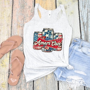 Puede incluir: Una camiseta sin mangas gris claro con un gráfico de tres latas de cerveza decoradas con la bandera estadounidense y el texto "Ameri Can". La imagen también incluye un par de chanclas rosas y unos shorts vaqueros.