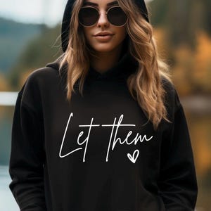 以下が含まれることがあります： 黒いフード付きスウェットシャツに、白い筆記体で「Let them」という文字と小さなハートのシンボルが書かれています。