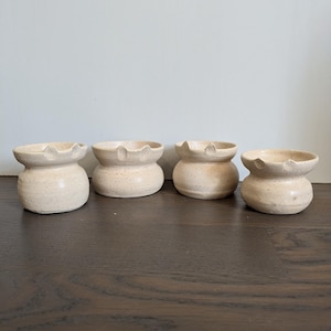 May include: Four small, white ceramic bowls with a speckled texture. The bowls have a rounded base and a flared rim.