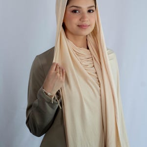 K&ouml;nnte beinhalten: Eine Frau tr&auml;gt einen hellbeigen Hijab mit einem lockeren, flie&szlig;enden Stil. Der Hijab ist &uuml;ber Kopf und Schultern gelegt und erzeugt einen weichen und eleganten Look.