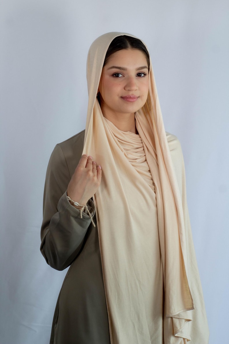 K&ouml;nnte beinhalten: Eine Frau tr&auml;gt einen hellbeigen Hijab mit einem lockeren, flie&szlig;enden Stil. Der Hijab ist &uuml;ber Kopf und Schultern gelegt und erzeugt einen weichen und eleganten Look.