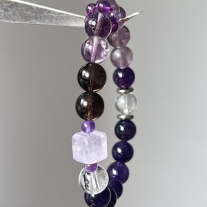 Hand holding the amethyst bracelet to showcase bead clarity and size.