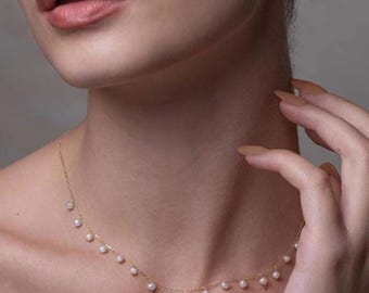 Puede incluir: Un delicado collar de cadena dorada con una serie de pequeñas perlas blancas espaciadas uniformemente y suspendidas a lo largo de la cadena. El collar descansa sobre el cuello, mostrando un diseño sencillo con una fina estructura de eslabones.
