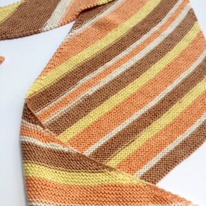 May include: A striped knitted scarf in shades of brown, peach, yellow, and white.