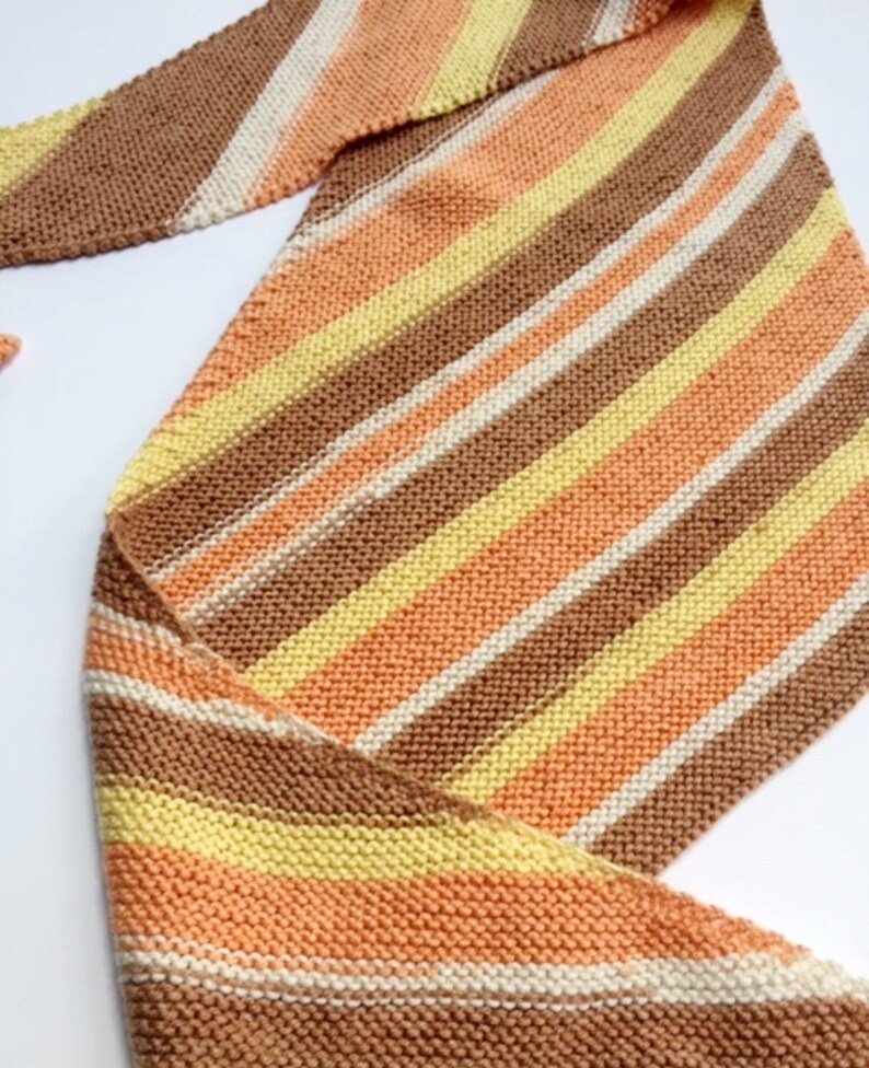 May include: A striped knitted scarf in shades of brown, peach, yellow, and white.