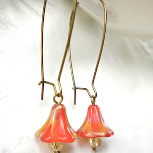 Puede incluir: Un par de pendientes colgantes con abalorios en forma de campana de vidrio naranja y amarillo y ganchos de color dorado.