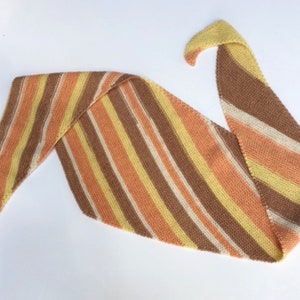 May include: A striped knitted scarf in shades of brown, orange, yellow, and white. The scarf is folded in a triangular shape.