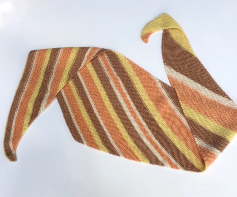 May include: A striped knitted scarf in shades of brown, orange, yellow, and white. The scarf is folded in a triangular shape.