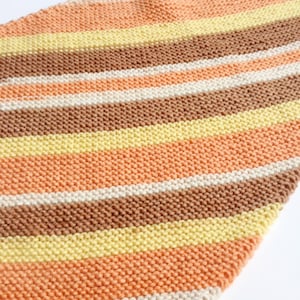 May include: A striped knitted scarf in shades of brown, peach, cream, and yellow.