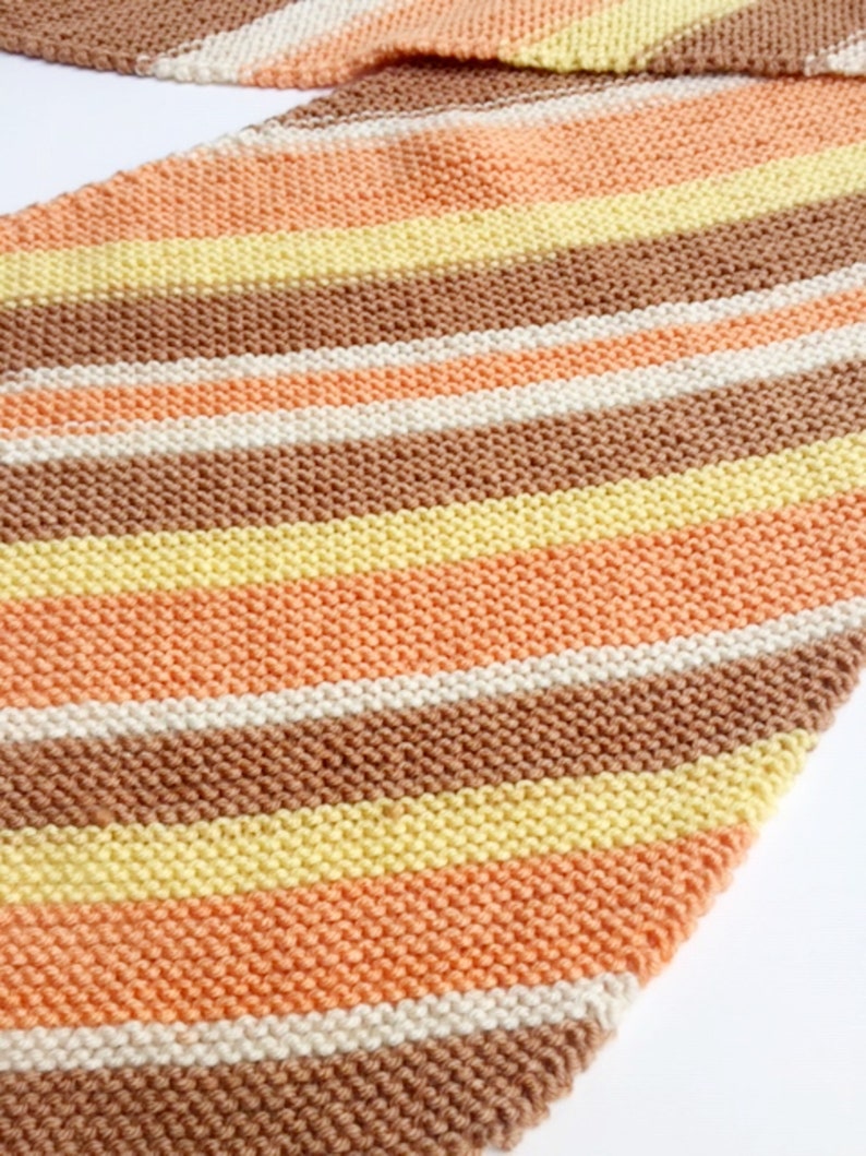 May include: A striped knitted scarf in shades of brown, peach, cream, and yellow.