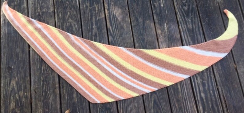 May include: A triangular shawl with diagonal stripes in shades of peach, yellow, and brown.