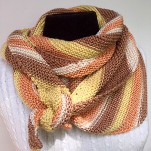 May include: A knitted scarf in shades of brown, orange, yellow, and white. The scarf is folded and tied in a knot.