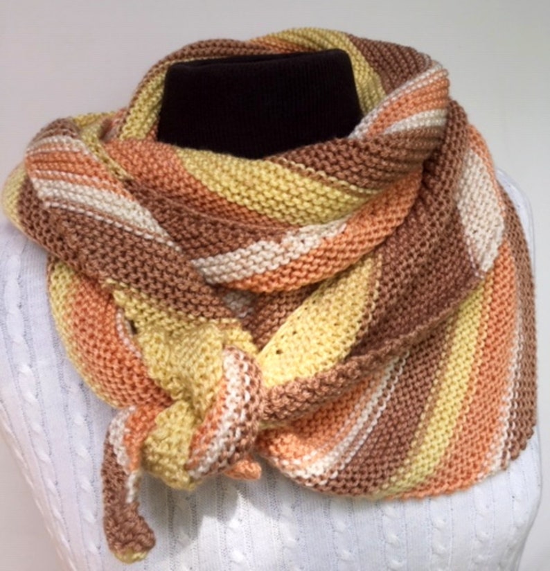 May include: A knitted scarf in shades of brown, orange, yellow, and white. The scarf is folded and tied in a knot.