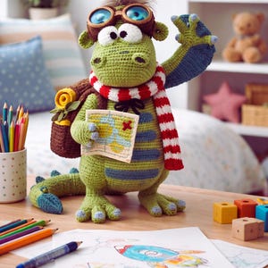 Peut inclure: Un jouet de dragon vert crochet&eacute; portant des lunettes d'aviateur, une &eacute;charpe ray&eacute;e rouge et blanche et un sac &agrave; dos. Le dragon tient une carte et se tient sur une table en bois &agrave; c&ocirc;t&eacute; d'un dessin de fus&eacute;e. Un porte-crayons avec des crayons est &agrave; gauche.